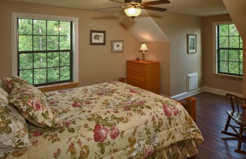 The image features an inviting bed decked with a comforter adorned in soothing floral patterns, nestled within our beautifully crafted log home.