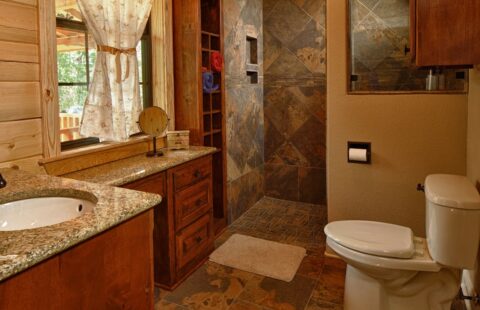 The image portrays a well-appointed bathroom in one of our log homes, complete with a toilet, sink, and a window.