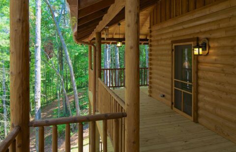 The image displays one of our beautifully crafted log homes featuring a robust wooden porch adorned with a sturdy wooden railing.