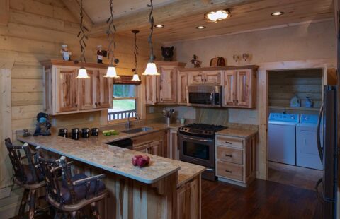 The image showcases the cozy, rustic elegance of our log home featuring a kitchen adorned with wood cabinets and counter tops.