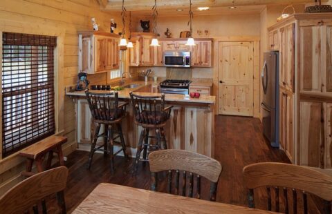 The image showcases a beautifully crafted, rustic log cabin interior featuring a fully equipped kitchen and cozy dining area.