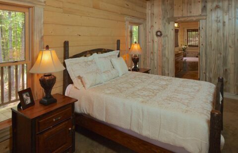The image showcases a cozy bedroom in one of our stunning log homes, featuring a comfortable bed and two rustic nightstands.