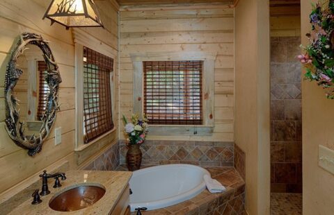 The image showcases a rustic, yet modern, bathroom inside our log cabin featuring a sleek tub and sink set amidst the natural warmth of wooden interiors.