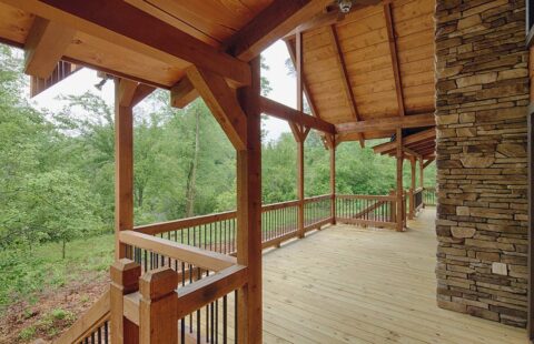 The image showcases a beautifully crafted wooden porch from one of our log homes, offering serene views of the surrounding forest.