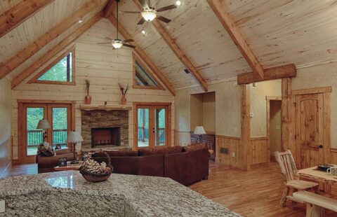The image displays a warm and inviting open-plan living room and kitchen area artfully crafted in one of our high-quality log cabins.