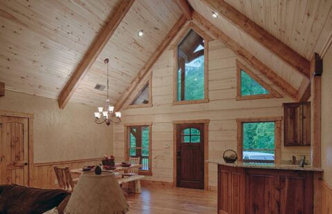 The image showcases a cozy, rustic log cabin featuring a beautifully arranged living room and dining area with wooden furnishings and warm, inviting interior design.