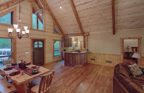 The image showcases a warm, inviting living room and dining area with exposed log walls and rustic furnishings crafted from natural materials within one of our beautifully designed log cabins.