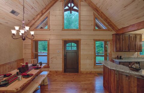 The image features a rustic, beautifully designed kitchen inside one of our log homes, complete with a wooden table and chairs.