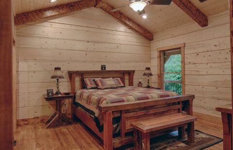 The image showcases a cozy bedroom within our log cabin, featuring a comfortable bed and a classic wooden bedside table.
