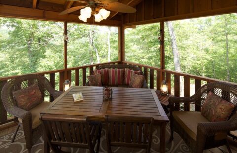 The image features a cozy screened-in porch of our log home, furnished with a stylish table and chairs for outdoor relaxation.