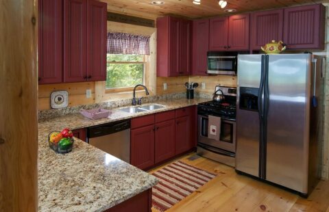 Our log home design features a stunning kitchen with vibrant red cabinets and high-quality stainless steel appliances.
