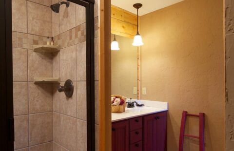 The image showcases a beautifully crafted, rustic bathroom within our log home, featuring a spacious shower and an elegant sink.