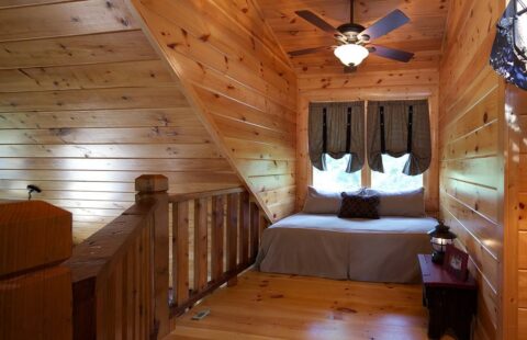 The image showcases a cozy bedroom in one of our log cabins, equipped with a comfortable bed and a ceiling fan for cooling.