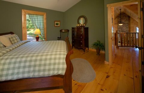 The image showcases a cozy, log-crafted bedroom featuring serene green walls and a comfortable bed.