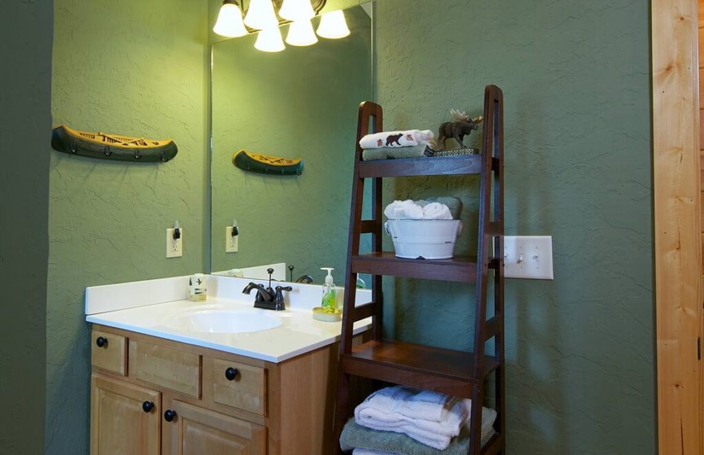 The image showcases a chic bathroom featuring a wooden ladder display complemented by soothing green walls for a rustic, yet modern appeal.