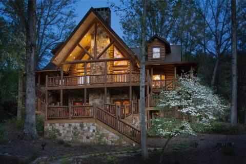 The image showcases one of our meticulously crafted log cabins nestled in a serene woodland landscape, radiating warm lights into the tranquil night.