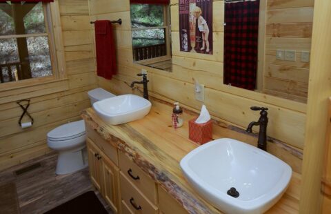 The image features a rustic, well-designed bathroom in one of our log cabins, equipped with two sinks and a toilet.
