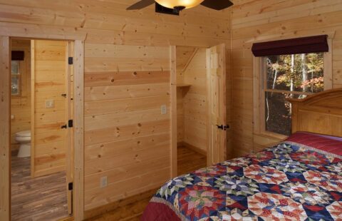 The image showcases a cozy bedroom within our beautifully crafted log cabin, complete with a comfortable bed and an overhead ceiling fan.