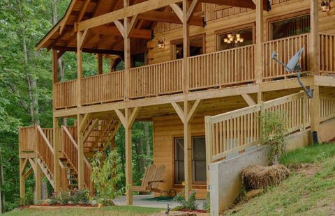 The image showcases a beautifully crafted log cabin perched on a serene hillside, complete with intricate wood detailing and accompanying stairs.