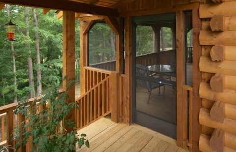 The image showcases a beautifully crafted log cabin featuring a spacious porch enclosed with a protective screen.