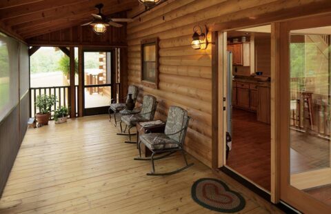The image showcases a rustic wooden porch of one of our log homes, complete with inviting rocking chairs and a modern sliding glass door.
