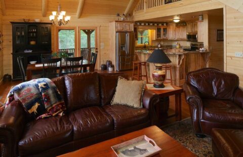 The image showcases a cozy living room in one of our premium log cabins, featuring exposed wooden beams, a roaring fireplace and chic rustic decor.