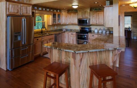 The image showcases a beautifully designed kitchen featuring our handcrafted wooden cabinets and countertops enhancing the cozy ambiance of a log home.