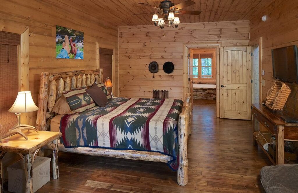 The image showcases a cozy bedroom within our beautifully-crafted log cabin, featuring a comfortable bed and state-of-the-art flat screen TV.