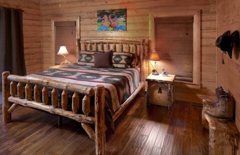 The image portrays a cozy bedroom in one of our log cabins, showcasing wooden floors and a comfortable bed.
