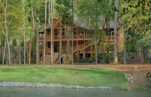 The image showcases a beautifully crafted log cabin nestled in the serene woods, majestically situated by a tranquil body of water.