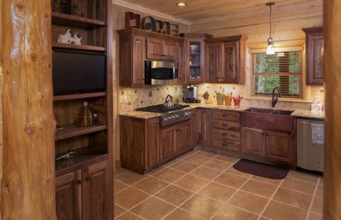 The image showcases an inviting kitchen area within our beautifully crafted log cabin, complete with wooden cabinets and a TV for a cozy and modern living experience.