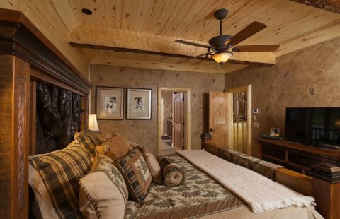 The image portrays a cozy bedroom in one of our log homes, equipped with a comfortable bed and an installed ceiling fan.