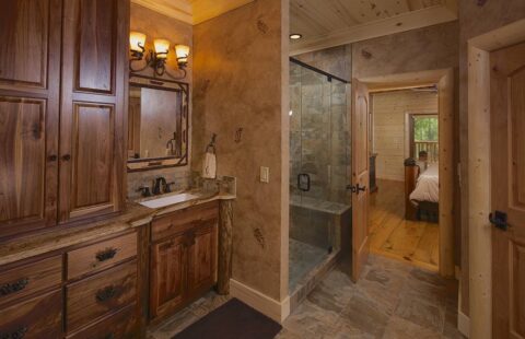 The image showcases a rustic-style bathroom featuring beautifully crafted wood cabinets and an accessible walk-in shower, reflecting our company's expertise in designing log homes.