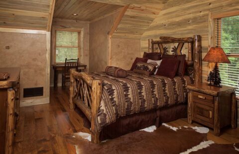The image showcases a cozy, rustic bedroom in one of our log homes, featuring a comfortable bed and an eye-catching cowhide rug enhancing the natural ambiance.