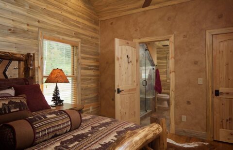 The image presents a cozily designed bedroom within one of our log homes, complete with a comfortable bed and an adjoining shower facility.