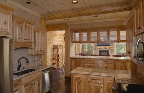 The image showcases a beautifully crafted kitchen within our log home, featuring rich wooden cabinets and striking granite countertops.