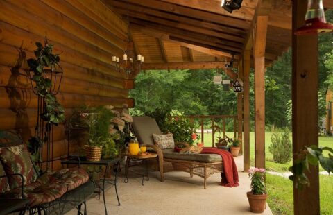 The picture showcases a beautifully adorned porch of one of our log cabins featuring lush plants and cozy, rustic furniture.