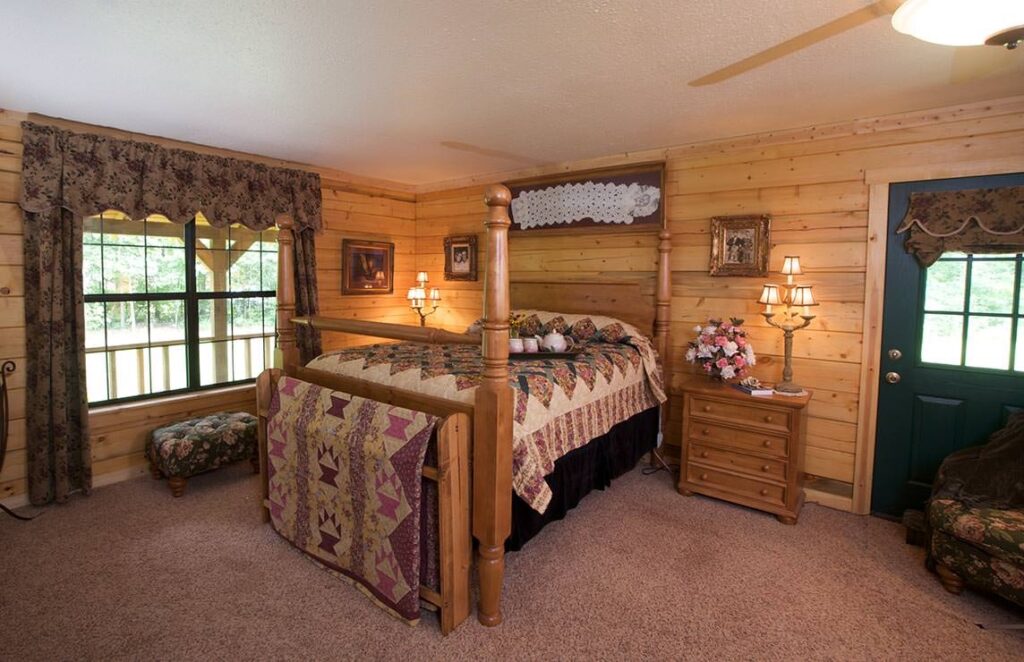 The image showcases a cozy bedroom within our beautifully crafted log cabin, featuring a timeless four-poster bed and warm wooden interiors.