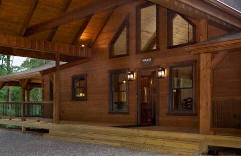 The image captures the enchanting view of a log home's front porch, beautifully illuminated as twilight descends.