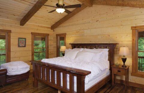 The image showcases a cozy bedroom in one of our meticulously crafted log cabins, complete with a comfortable bed and an overhead ceiling fan.