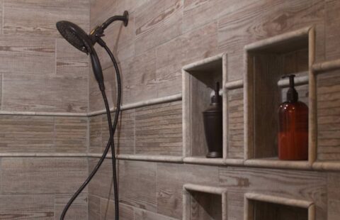 The image depicts a beautifully crafted bathroom featuring a unique wooden shower head and matching wooden shelves, demonstrating our company's commitment to innovative log home construction.