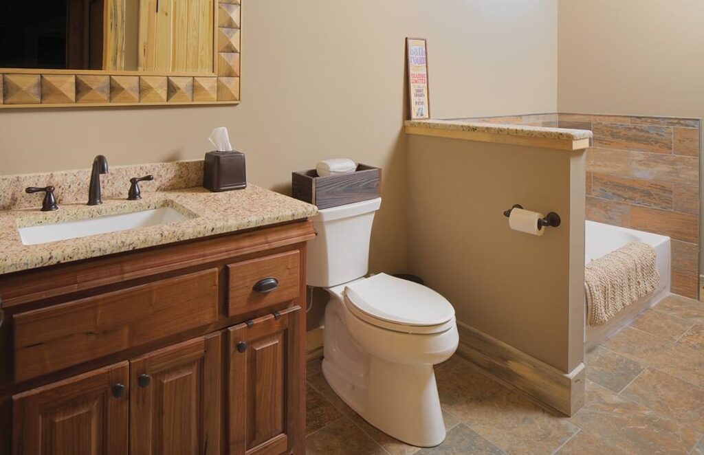 The image showcases a cozy bathroom in one of our log homes featuring a toilet, sink and mirror, exuding rustic charm and modern functionality.