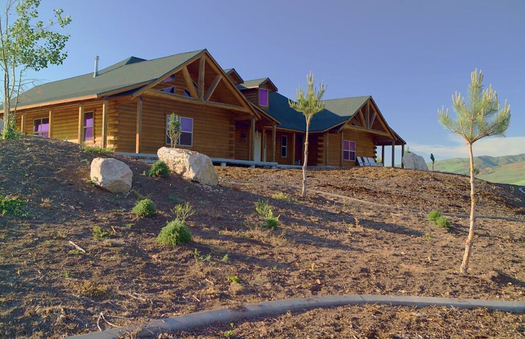 The image depicts a beautifully crafted log home majestically situated on a hill.