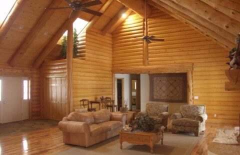 The image showcases a cozy and rustic living room within our high-quality log cabin, complete with sturdy wooden furniture, roaring fireplace, and large windows for ample natural light.
