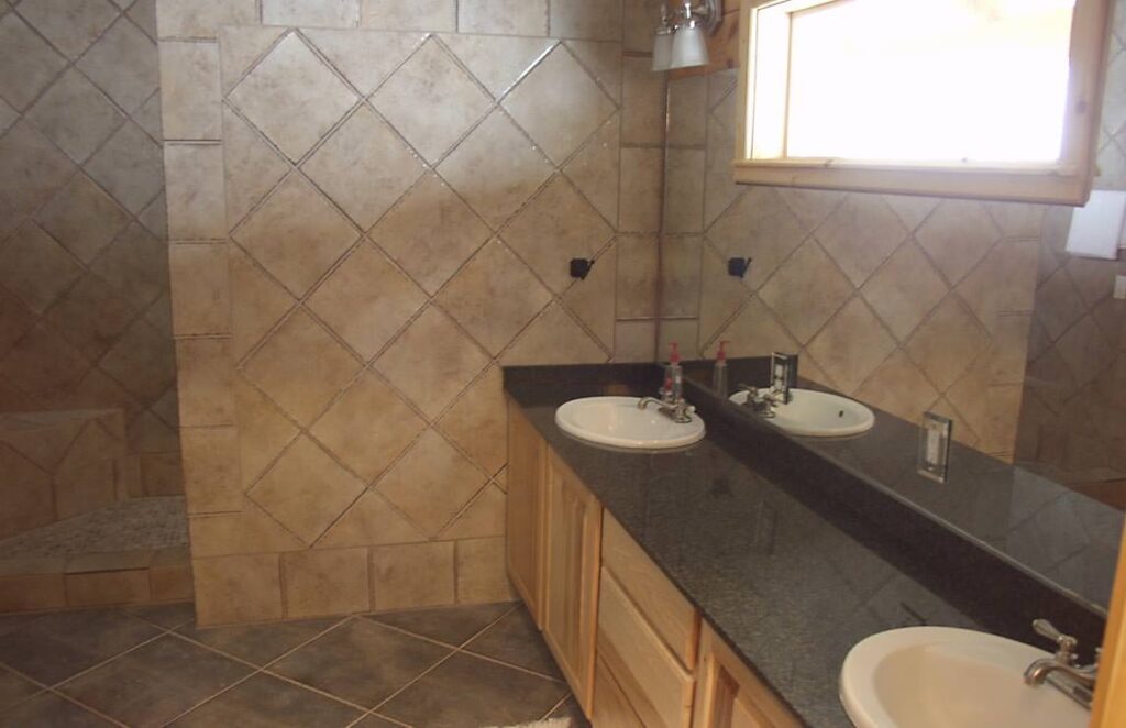 The image showcases a beautifully designed bathroom in one of our log homes, featuring dual sinks and a luxurious shower.