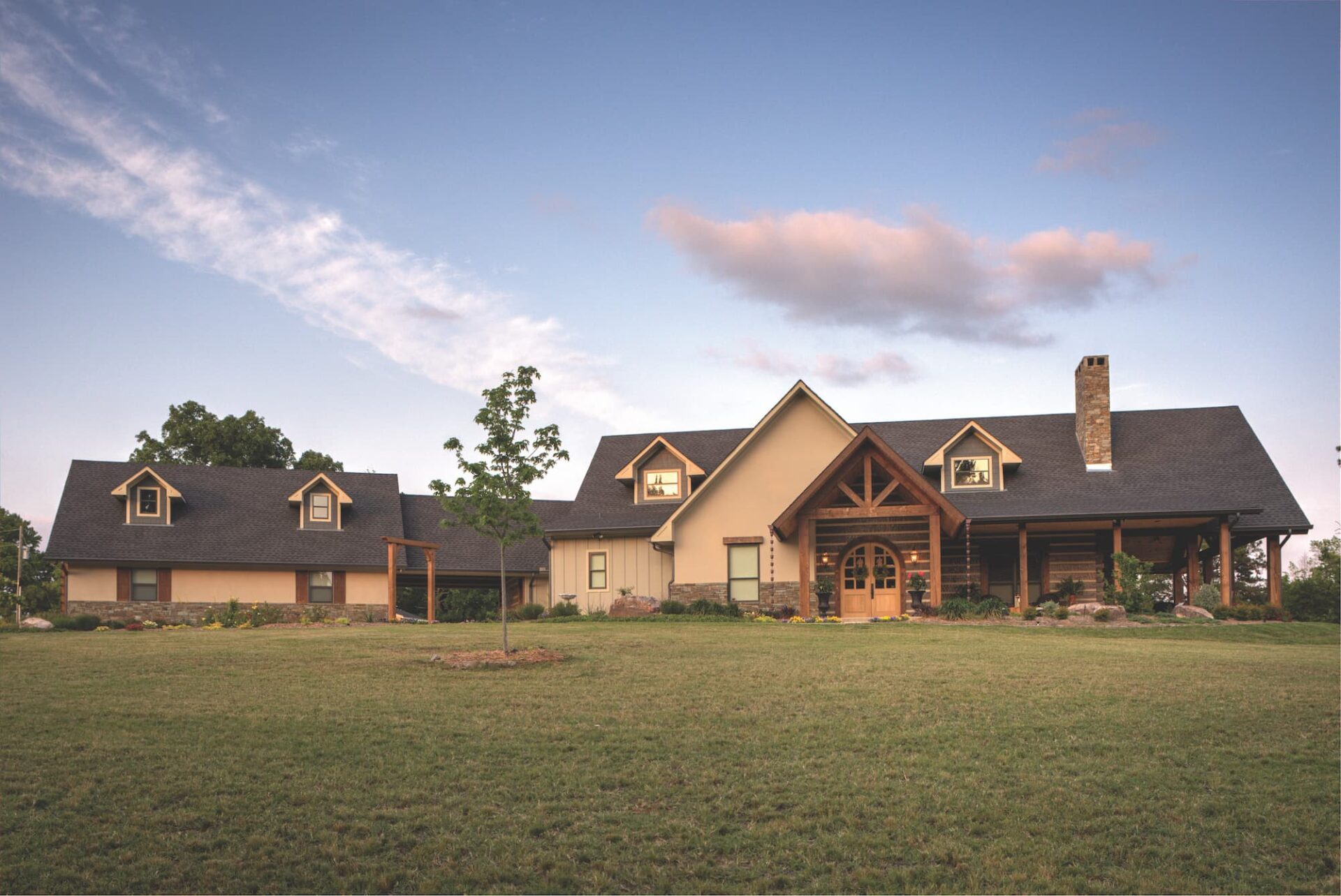 Our company creates exquisite, large brown log homes nestled beautifully in lush green fields.