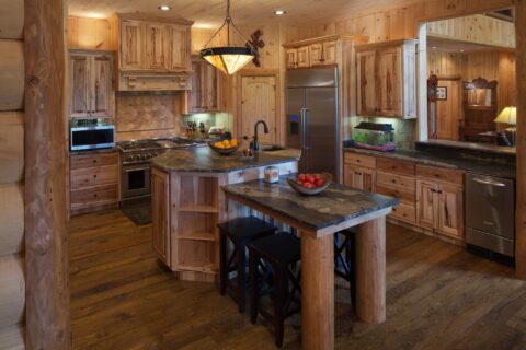 The image portrays a beautifully crafted, rustic kitchen featuring our high-quality wood cabinets and an inviting center island, epitomizing the charm of log home living.