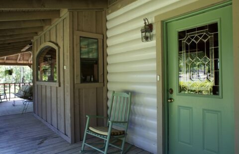 The image showcases a rustic log home featuring a welcoming porch adorned with a vibrant green door and a classic rocking chair.