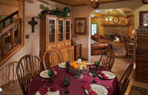 The image showcases a cozy dining room interior within our expertly constructed log cabin, featuring a roaring fireplace.
