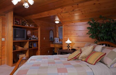 The image showcases a well-appointed bed set in the comforting rustic elegance of one of our log home bedrooms.